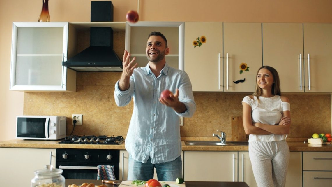 Attractive loving couple having fun in the kitchen. Handsome man juggle with apples to impress his girlfriend at home