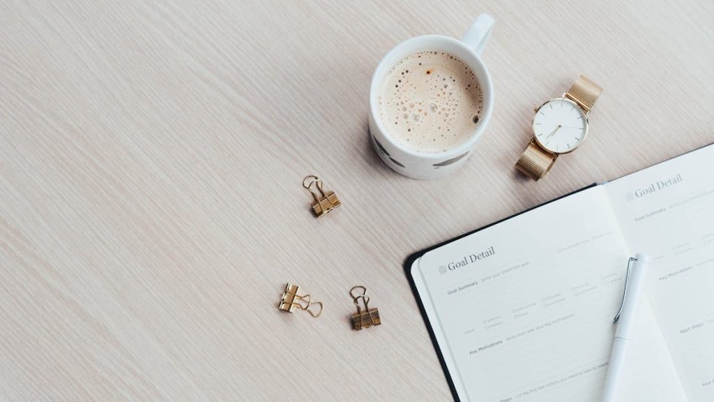 A minimalist desk arrangement featuring a coffee cup, notebook, pen, and wristwatch.