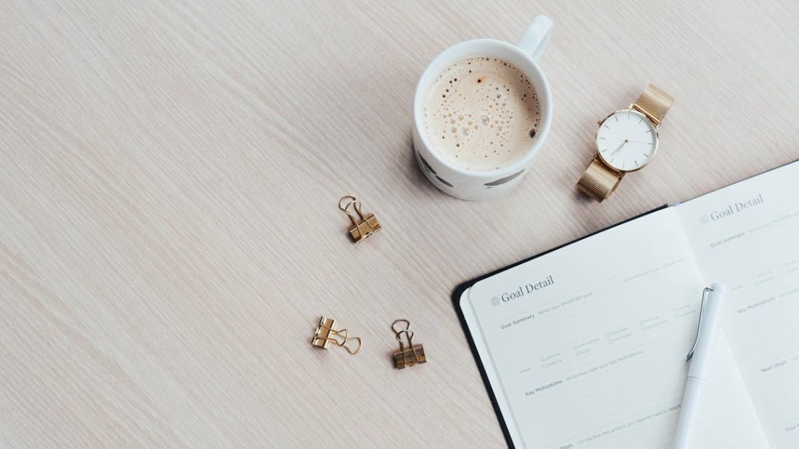 A minimalist desk arrangement featuring a coffee cup, notebook, pen, and wristwatch.