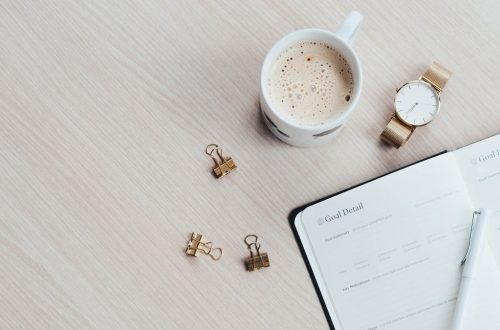 A minimalist desk arrangement featuring a coffee cup, notebook, pen, and wristwatch.